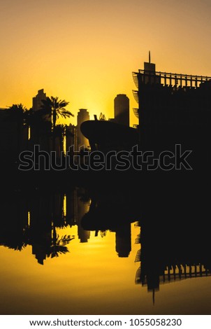 skyscrapers and palms reflected in the water against the sunset in Dubai