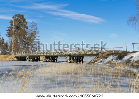 Beautiful nature and landscape photo of sunny spring day in Sweden Scandinavia Europe. Nice outdoors image with ice lake, trees, blue sky and wooden bridge. Calm, peaceful and happy background picture