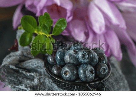 Ripe blueberry and blueberry in a metal Cup against the background of delicate flowers timeless. Close up.