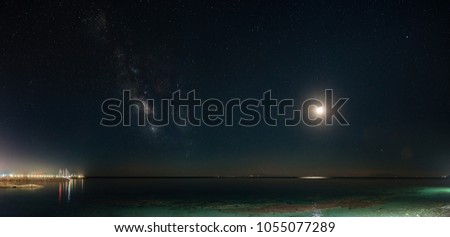 Panoramic Milky Way galaxy and young moonset. Milky Way galaxy over the seacoast with moonset, small harbor on the left side. The night sky is astronomically accurate.