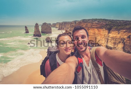 handsome couple backpackers take selfie in front of the cliff of twelve apostles on the ocean of Victoria region in a summer day, Victoria, Australia. Royalty-Free Stock Photo #1055091110