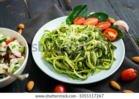 Zucchini raw vegan pasta with avocado dip sauce, spinach leaves and cherry tomatoes on plate. On dark background. Vegetarian healthy food Royalty-Free Stock Photo #1055117267