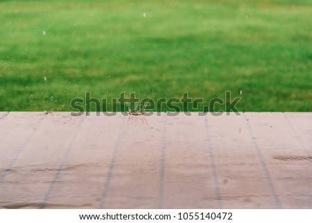 Rain drops falling to wooden floor and blurred green grass background.High speed shutter.Rainy season concept.Selective focus.