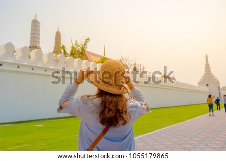 woman traveler with bag cross body and hat look at the temple “wat phra kaew” and background from Bangkok Thailand. Traveling Thailand.