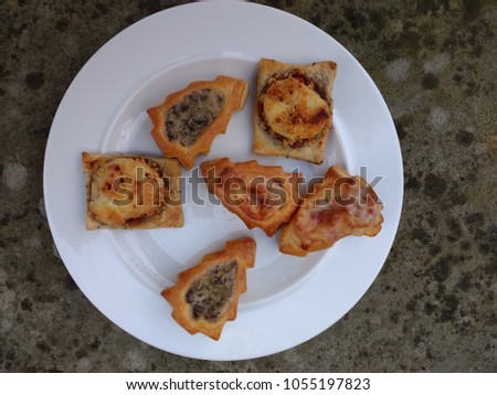 Close up of party food of delicious tasty canapé snacks hot from oven on white plate set on antique stone grey background of puff pastry shapes of Christmas tree with cheese and savoury filling