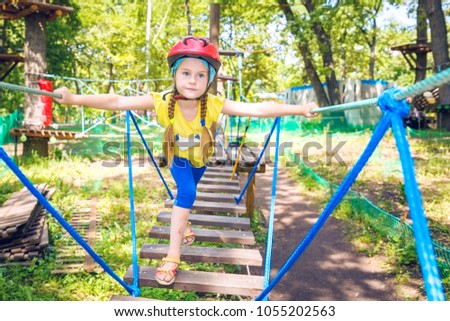A little girl is climbing on a cableway of obstacles in a city park.