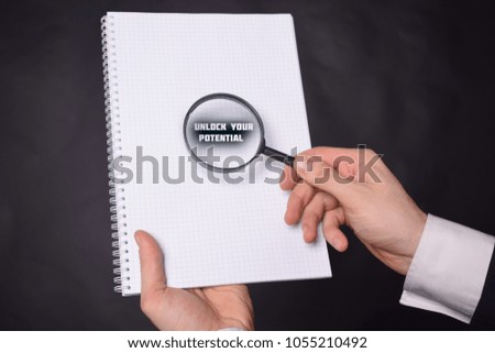 Businessman looking at a magnifying glass word:UNLOCK YOUR POTENTIAL