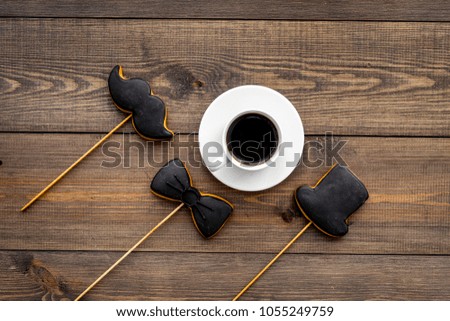 Men's birthday celebration concept. Cookies in shape of moustache, hat, bow tie near coffee on dark wooden background top view
