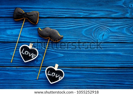 Happy Father's Day. Greetings and presents concept. Cookies in shape of moustache, hat, bow tie and hearts with lettering love you on blue wooden background top view copy space