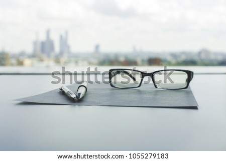 Close up of table with glasses, paper sheet and pen on blurry city background