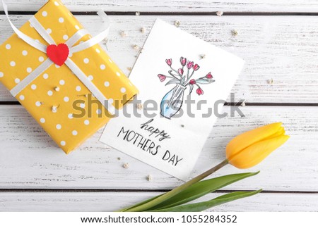 Greeting card with phrase "Happy  Mother's day" and gift box on table
