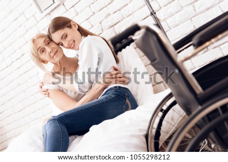 Girl is nursing elderly woman in bed at home. They are hugging each other.
