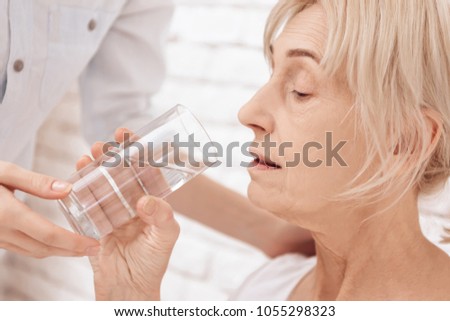 Close up. Girl is caring for elderly woman in bed at home. Girl is helping woman with glass of water.
