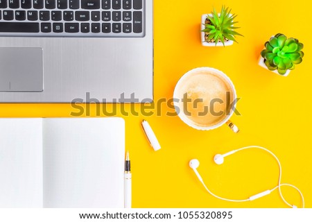 Workplace with a laptop, bkllonotom, pen, headphones, a cup of coffee and green whiskers in white pots. The working space of a freelancer, journalist, writer. On a bright yellow background. Top view. Royalty-Free Stock Photo #1055320895