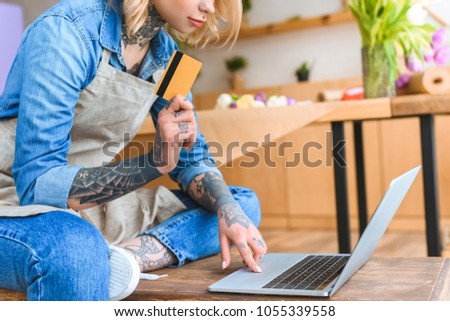 cropped shot of young florist holding credit card and using laptop