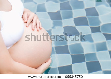 pregnant woman relax by the pool and touching her belly with hands