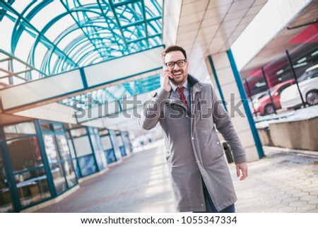 Businessman using mobile phone outside of office buildings in the background. Young caucasian man holding smartphone for business work.
