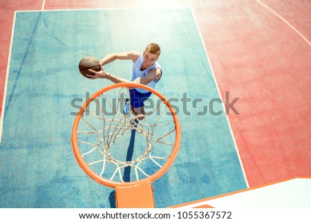 Young man jumping and making a fantastic slam dunk playing streetball, basketball. Urban authentic.
