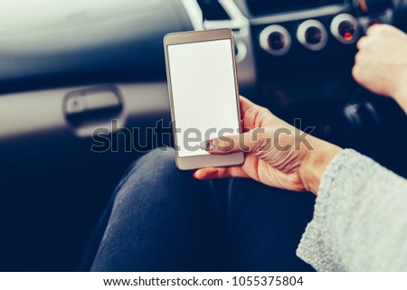 Stylish gold smartphone in the hand of a girl in the car. A young woman driver using the phone's touch screen and GPS navigation in the car. Use the phone while driving. Stylish toned photo