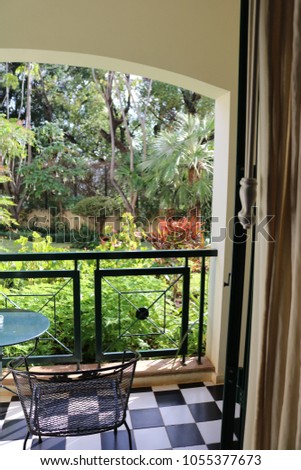 View Of Lush Garden With Trees And Bushes Through Open Door Across Black And White Tiled Terrace With Railings - Image