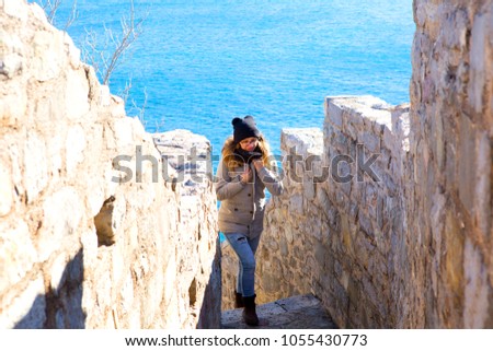 Beautiful girl climbing stairs besides stone walls, in background is the blue sea. Budva, Montenegro