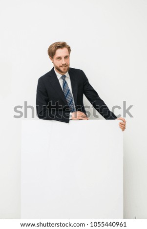 confident elegant handsome blonde man in suit, businessman or salesman, standing on white background with empty panel with free space for text, looking to camera with joy and confidence