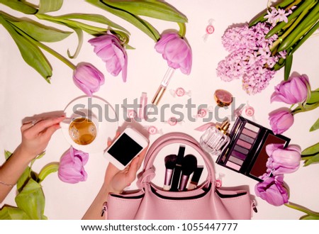 woman's hand holds a cup of coffee and a phone on a background with flowers and decorative cosmetics, macro photography