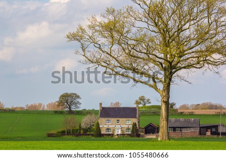 English country cottage farmhouse. Idyllic secluded countryside farm house building in a field under a tree. Beautiful picture book home.
