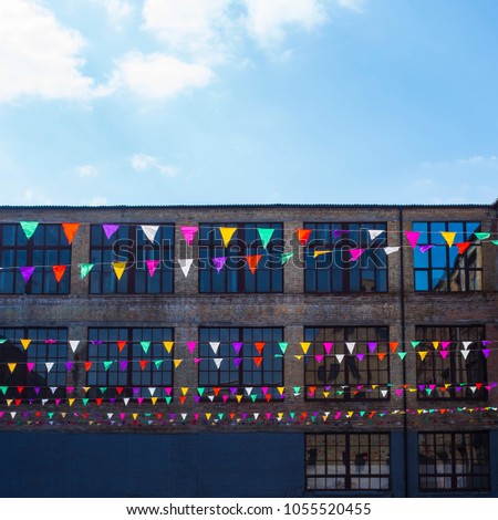Multicolored triangular decorative flags hang on the background of old loft brick buildings with large windows. Background, copyspace
