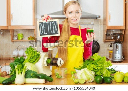 Drinks good for health, diet breakfast concept. Young woman in kitchen making green healthy vegetable smoothie juice holding detoxsign