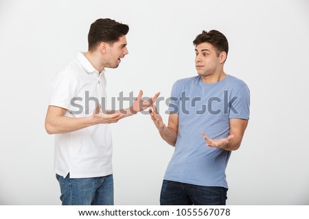 Portrait of two confused young men talking isolated over white background Royalty-Free Stock Photo #1055567078