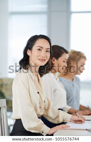 Smiling Chinese business lady taking notes at the meeting