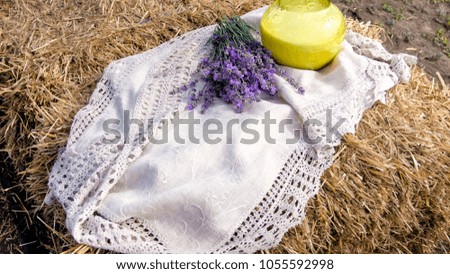 Closeup photo of bunch of lavender flowers and jar of milk on hay stack