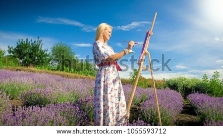 Beautiful woman in long dress painting picture on easel of lavender field