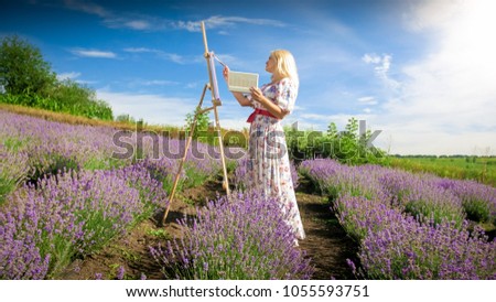 Blonde woman standing in lavender field and painting beautiful landscape