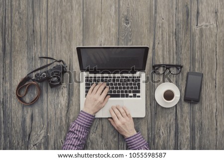 Hipster freelance working at office desk, he is networking and typing on a laptop, top view