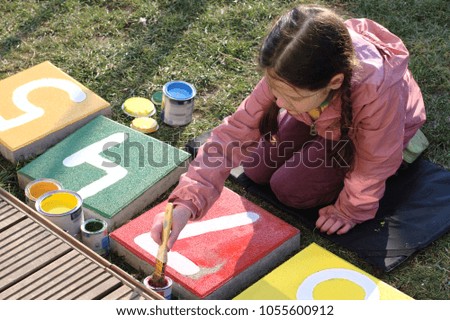 A little girl helps when working in the garden, paints concrete slabs, draws figures.