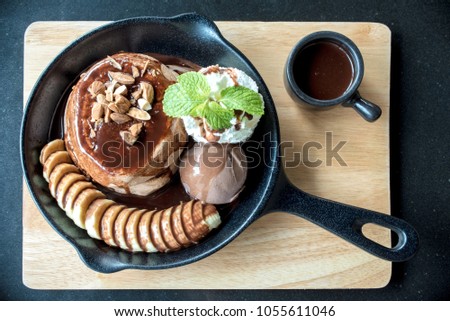 Delicious pancake with banana chocolate and vanilla ice cream on black iron pan over cock coaster.