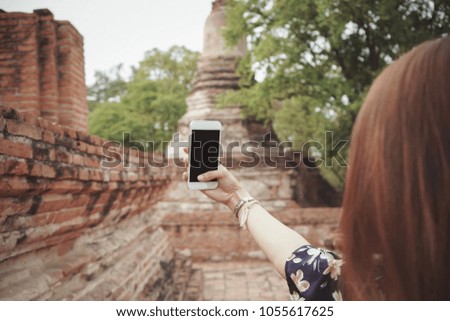 hand of beautiful girl holds the mobile phone and takes a picture with Temple in Ayutthaya Thailand background . selective focus .