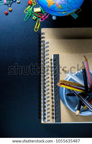 Education concept. Top view of brown notebook on floor with colorful equipment and pencils on black background with copy space for text. 