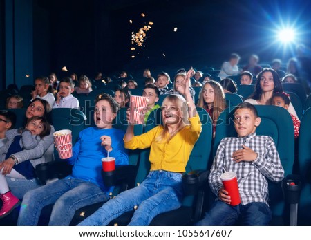 Photo of children sitting on first cinema row. Schoolmates very emotional,exited,surprised,happy and satisfied. girl wearing yellow cardigan spilling up popcorn by watching movie.