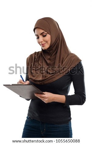 Arabian woman writing a report on her clipboard. Good attitude at work and positive thinking. Productive employee concept.