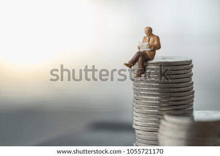 Business, Money and planning concept. Businessman miniature figure sitting and reading a newspaper on top of stack of silver coins.