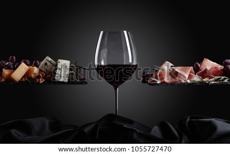 Glass of red wine with various cheeses , fruits and prosciutto on a black background. Royalty-Free Stock Photo #1055727470