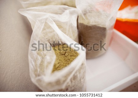 Close up picture of plastic transparent bags filled with green milled spice placed on a white basin.