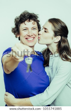 Closeup of young woman kissing and embracing her smiling senior mother holding keys. Isolated view on white background.