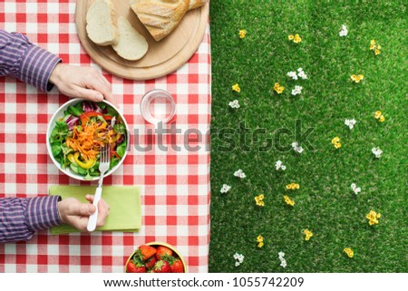 Man eating a salad on a checked tablecloth outdoors, picnic and healthy eating concept