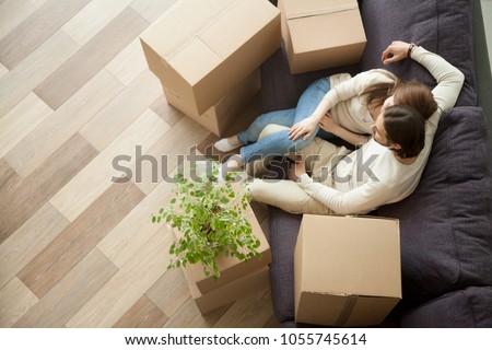 Young millennial couple owners moved into new home resting on couch on moving day, happy family with boxes relaxing on sofa in living room, easy relocation with delivery service concept, top view Royalty-Free Stock Photo #1055745614