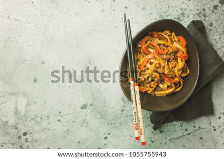 Asian food, stir fry udon noodles with meat and vegetables in a bowl on gray stone background, top view