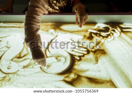 Girl in the game draws her fingers on the sand with a backlight